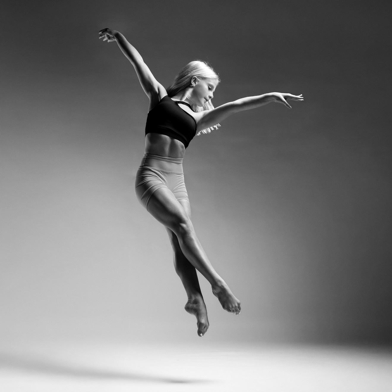 A person is gracefully leaping in a black and white image, showcasing dynamic movement and balance against a studio backdrop.