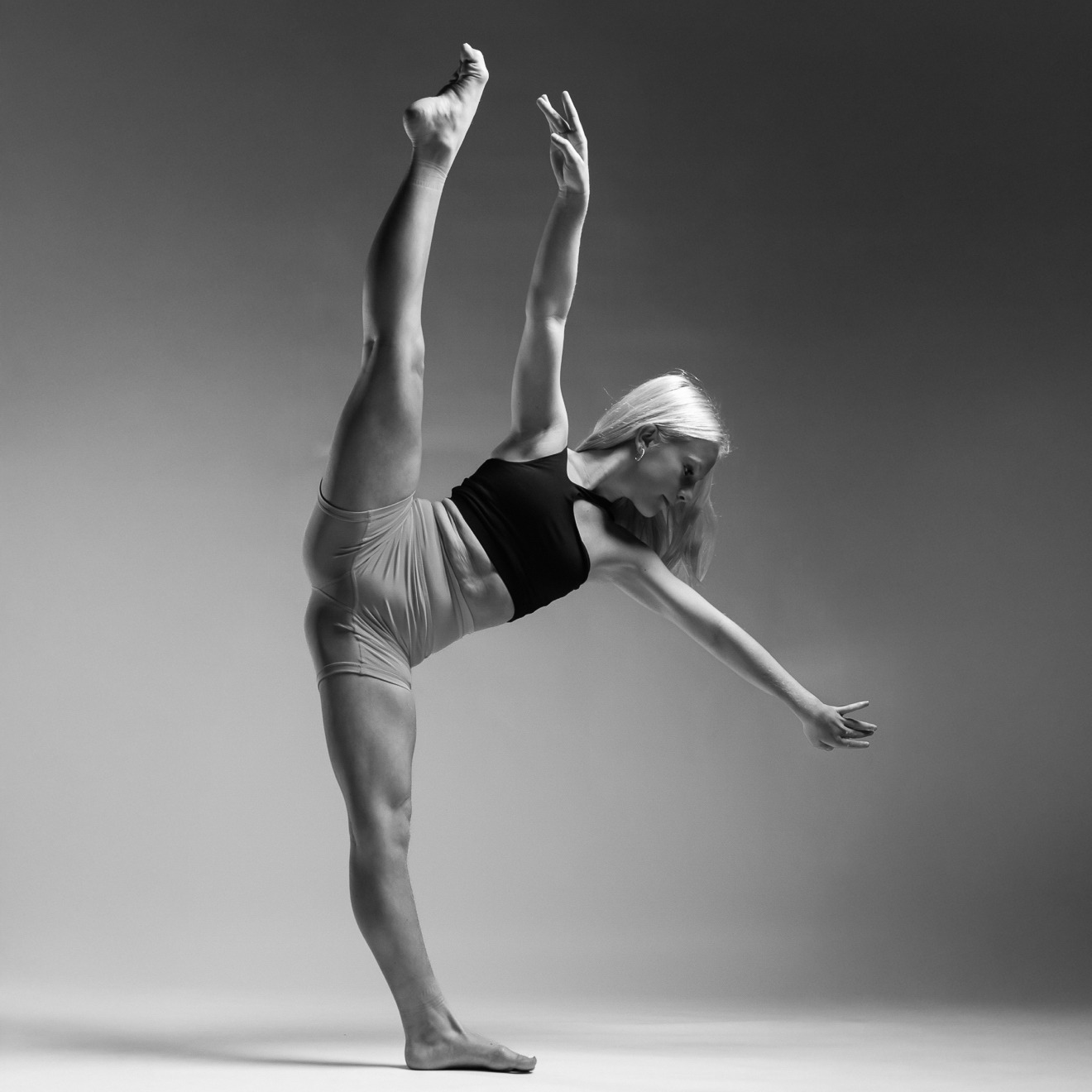 A person performs a high leg extension in a studio setting, showcasing graceful balance and flexibility in a monochrome photograph.